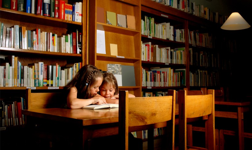 two girls sharing a book in a library