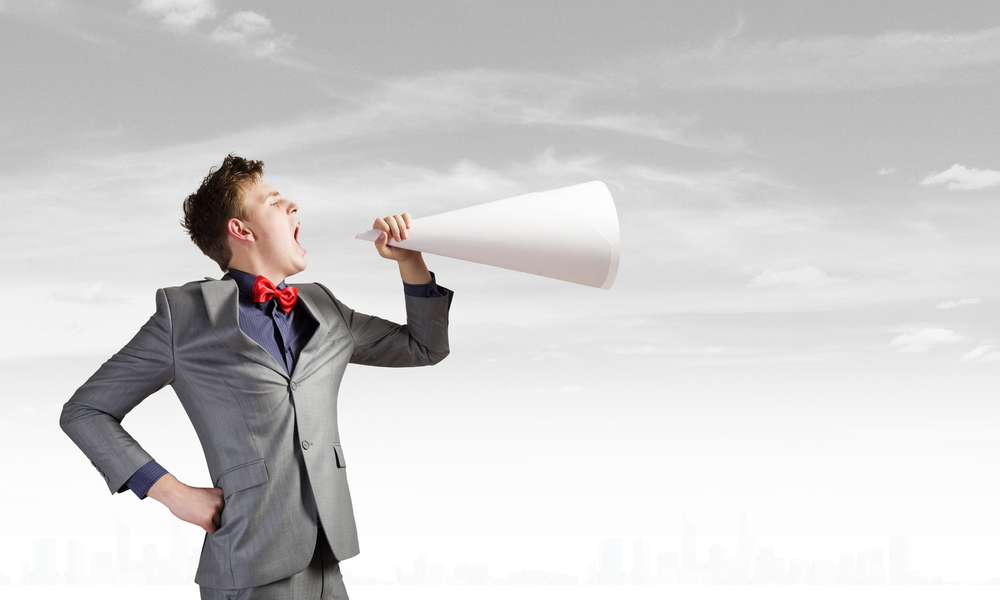 young man in business suit talking into a paper megaphone